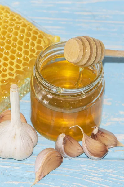 Honey and pieces of garlic on the background of honeycomb. Honey in a glass jar and honeycomb. — Stock Photo, Image