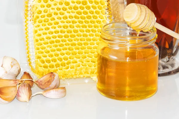 Honey and pieces of garlic on the background of honeycomb. Honey in a glass jar and honeycomb. — Stock Photo, Image