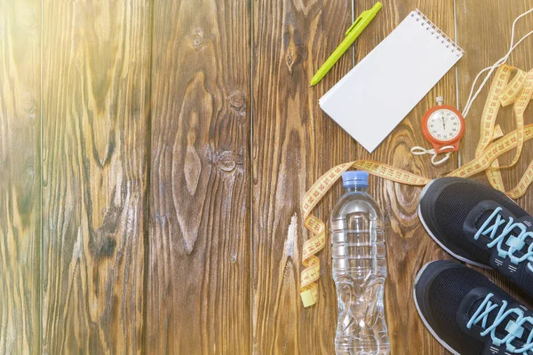 Estilo de vida saludable y antecedentes deportivos. Zapatillas deportivas, Bloc de notas y bolígrafo, cronómetro y botella de agua sobre fondo de madera con copyspace, vista superior . —  Fotos de Stock