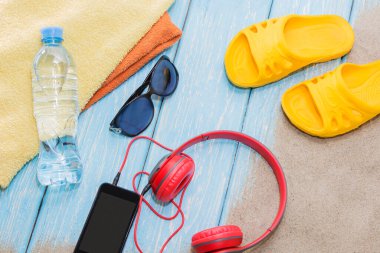 Bir şişe su ve parlak havlular, mavi arka planda sarı bir tahta ve güneş gözlüğü. Boşluğu Kopyala