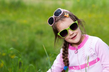 Gözlüklü küçük kız çimenlerde poz veriyor - bahar zamanı