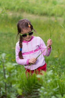 Gözlüklü küçük kız çimenlerde poz veriyor - bahar zamanı