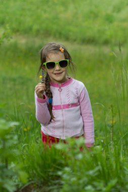 Gözlüklü küçük kız çimenlerde poz veriyor - bahar zamanı