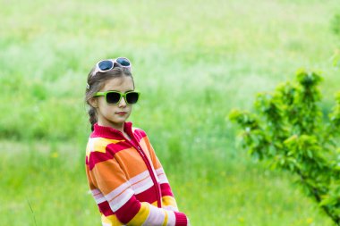 Gözlüklü küçük kız çimenlerde poz veriyor - bahar zamanı
