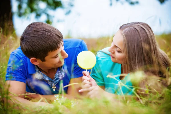 ロマンチックな若いカップル食べる黄色ロリポップは フィールドでのリラックス — ストック写真