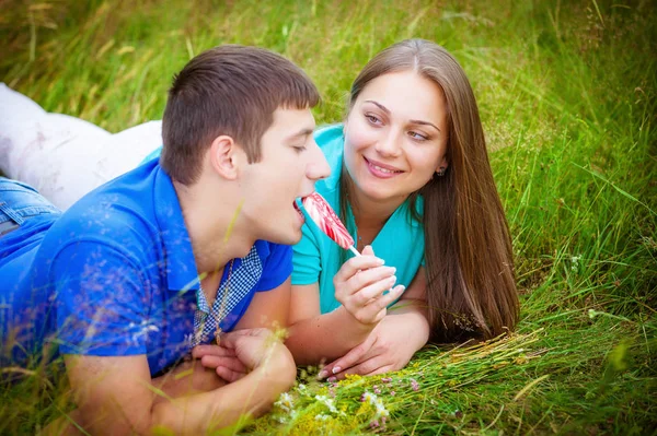ロマンチックな若いカップルはロリポップを持って女の子緑の草の上に横たわる — ストック写真