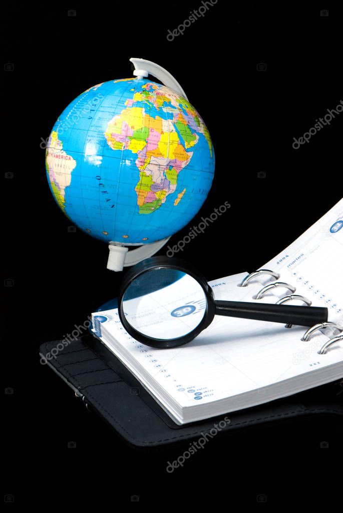 earth globe and notebook with magnifying glass on black background