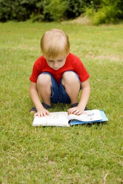 sevimli küçük çocuk Park yeşil çimenlerin üzerinde oturup kitap okuma