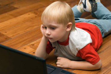 Dizüstü bilgisayar kullanarak ahşap yerde yatarken şirin sarışın çocuk portresi