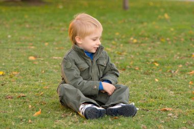 sarı sonbahar ile yeşil çimenlerin üzerinde oturan sevimli küçük çocuk bırakır