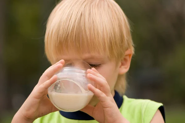 户外肖像可爱的小男孩喝牛奶站在模糊绿色背景 — 图库照片