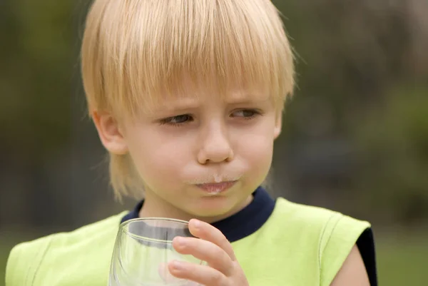 かわいい小さな少年飲酒ミルクの立っている上の屋外のポートレートは緑背景をぼかし — ストック写真