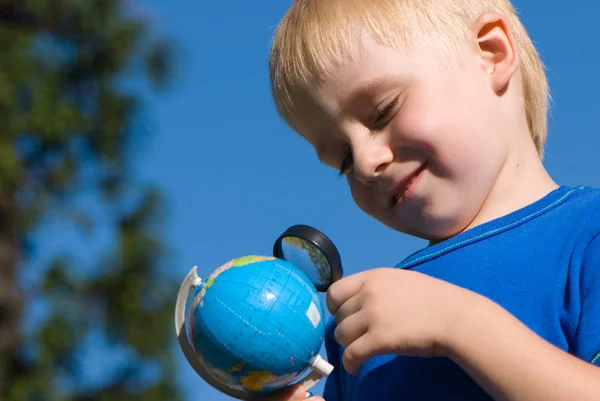 可爱的小男孩拿着地球仪 看着放大镜玻璃对抗蓝天背景 — 图库照片