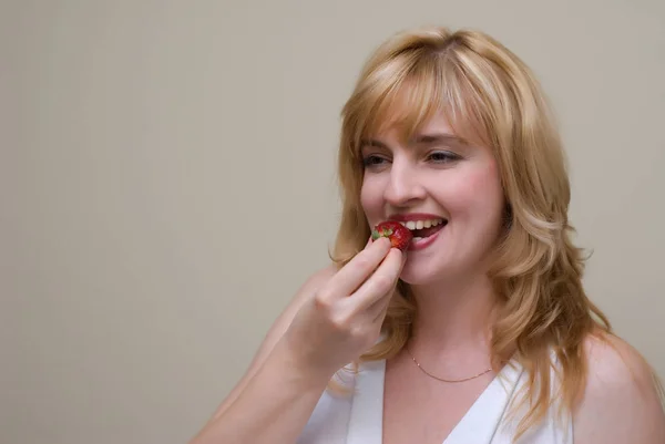 美丽的金发女郎微笑着吃草莓摆在米色工作室背景 — 图库照片