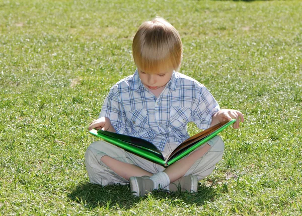 Netter Kleiner Junge Sitzt Auf Grünem Gras Und Liest Buch — Stockfoto