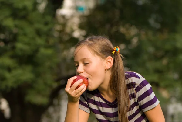 赤いリンゴを食べる少女の屋外のポートレート — ストック写真