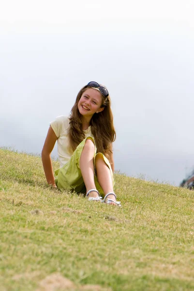 漂亮的少女长发和太阳镜坐在绿色的草地上 — 图库照片