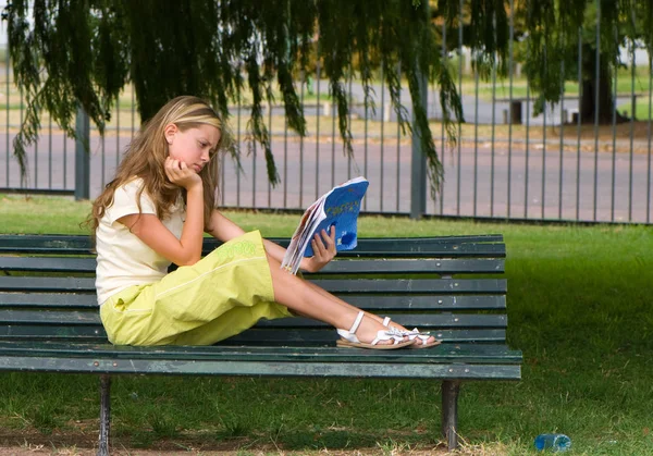 可爱的少女阅读书坐在长椅上的绿色公园 — 图库照片