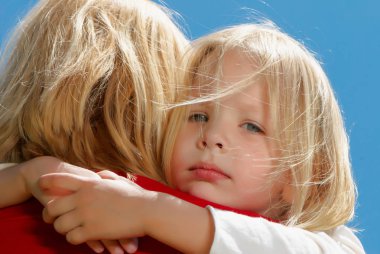 mavi gökyüzü önünde kucaklayan anne ve kızı portresi