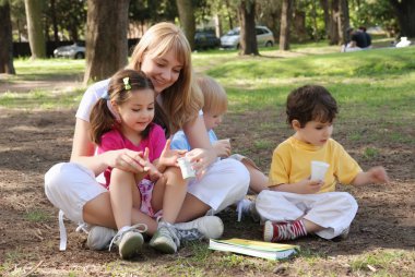 Genç bir kadın çocuklarla parkta vakit geçiriyor.