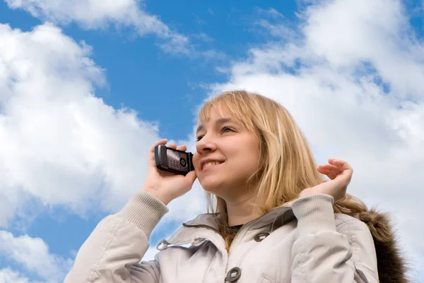在冬天夹克的女人的底部的看法 在天空前通过电话交谈 — 图库照片