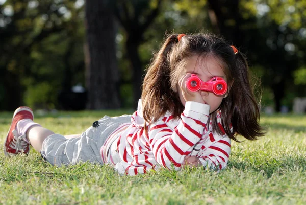 可爱的小女孩的肖像与玩具望远镜躺在草地上 — 图库照片