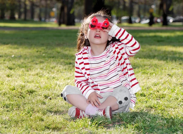 草の上に横たわっているおもちゃの双眼鏡を持つ愛らしい小さな女の子の肖像画 — ストック写真