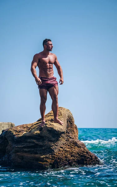 Όμορφος Αρσενικό Αθλητής Ποζάρει Πάνω Βράχους Μπροστά Στη Θάλασσα — Φωτογραφία Αρχείου