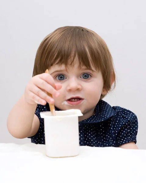 白い背景にヨーグルトを食べる濃い青のTシャツの小さな女の子の肖像画 — ストック写真