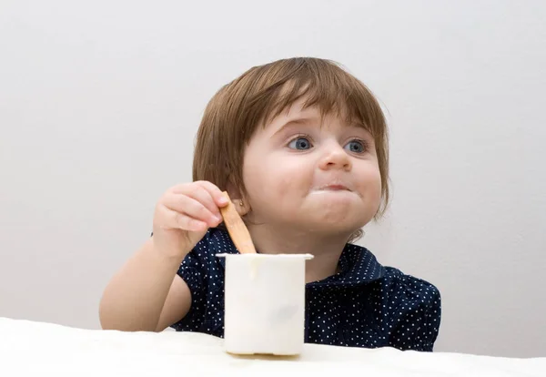 白い背景にヨーグルトを食べる濃い青のTシャツの小さな女の子の肖像画 — ストック写真