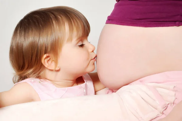 小女孩亲吻怀孕的母亲肚子在白色背景 — 图库照片