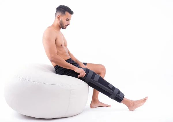 Young man in supportive leg brace posing on white background