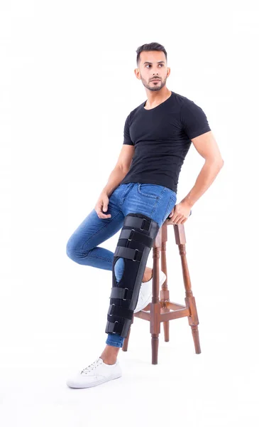 Young man in supportive leg brace posing on white background