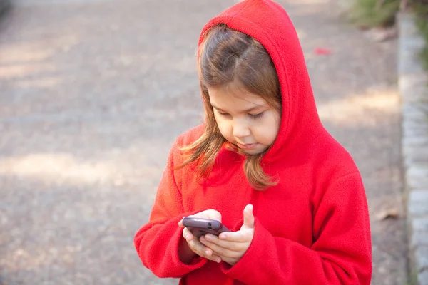 Flicka i rött med mobil i parken — Stockfoto