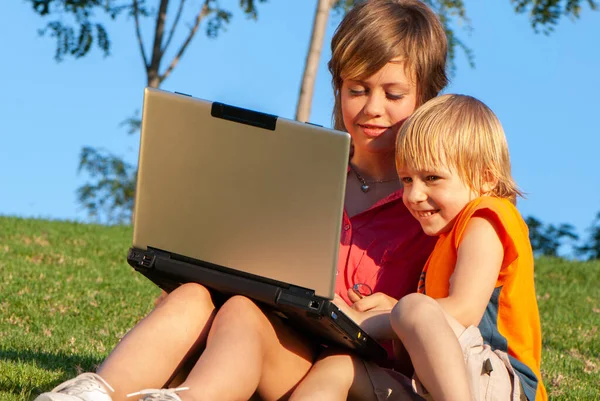 公園でコンピュータを手にした幸せな女の子と弟は — ストック写真