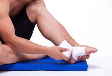 Beyaz arka planda genç bir adamın bacağına bandaj yapıştırıyorum.