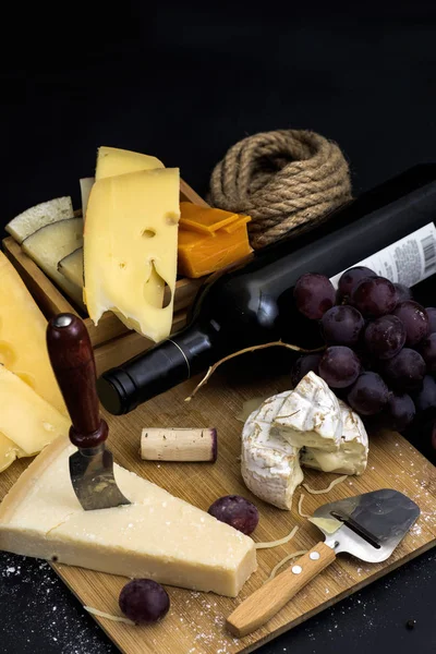 varied cheese on a black background on a wooden board with a knife