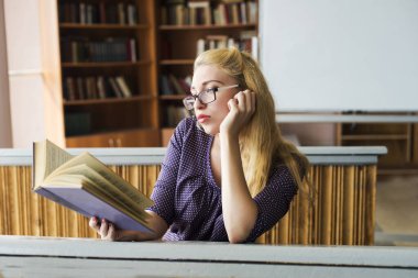 Kız öğrenci kütüphanede kitap okuyor.