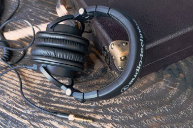 Ses-Teknik M-serisi kulaklıklar, klasik stil ve sarmalanmış kablolar. Stüdyo kalitesinde ses ekipmanları deri çantanın yanında dokulu ahşabın üzerinde dinleniyor..