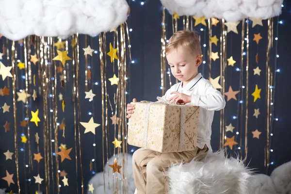 Симпатичный маленький мальчик с подарком в студии с золотыми звездами декора — стоковое фото