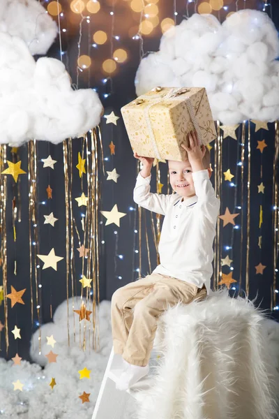 Menino bonito com um presente em um estúdio com uma decoração estrelas de ouro — Fotografia de Stock