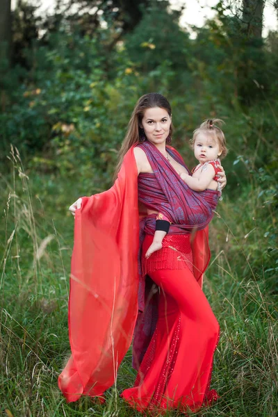 Mujer con traje de danza del vientre con su hija en un cabestrillo — Foto de Stock
