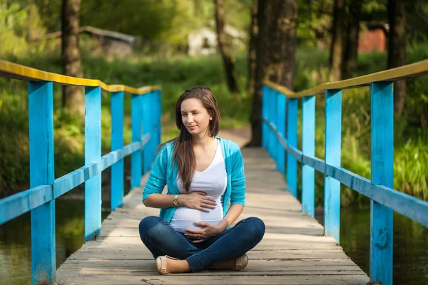 Porträt einer jungen glücklichen Schwangeren auf einer blauen Holzbrücke. — Stockfoto