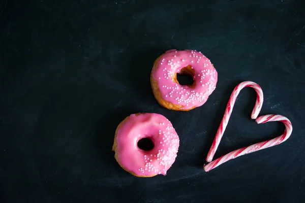 Ντόνατς και καρδιά από ζαχαροκάλαμο καραμέλα σε μαύρο φόντο — Φωτογραφία Αρχείου