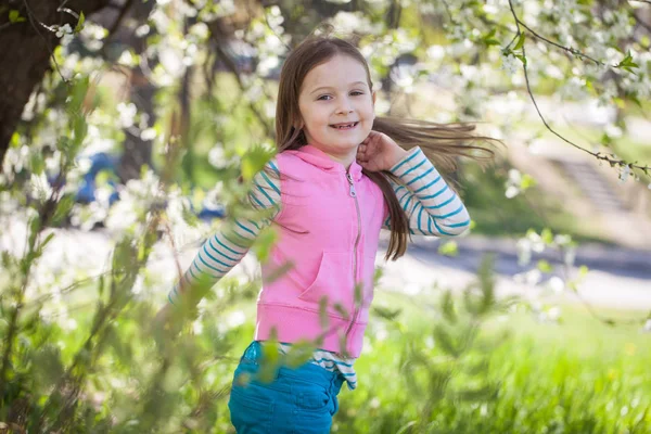 Menina bonito em um jardim de árvore de cereja florescendo — Fotografia de Stock