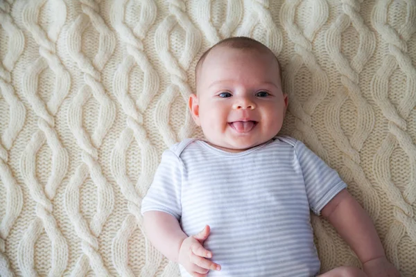快乐的婴儿在条纹紧身衣躺在她的背部上的羊毛毯子 并显示她的舌头 — 图库照片