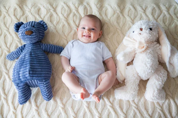 ウサギとクマのおもちゃで彼女の背中に横になっている笑顔の愛らしい赤ちゃん女の子 — ストック写真