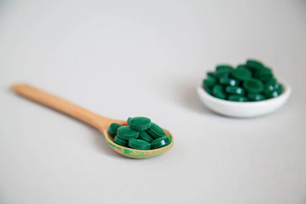 グレーの背景に緑のらせん状の丸薬と密接な木製のスプーン スーパーフードのコンセプト スピルリナの栄養補助食品 — ストック写真