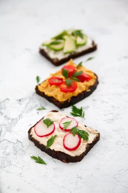 Yakın plan vejetaryen çavdar ekmeği tostları süzme peynir, humus, avokado, turp ve domates beyaz arka planda.