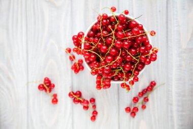 Tahta arka planda beyaz bir kasede taze, sulu, taze kırmızı kuşüzümü.